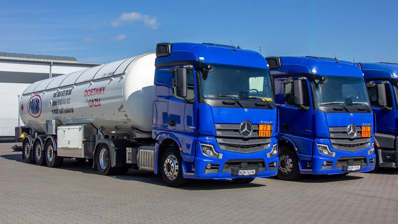Niebieskie ciągniki Mercedes-Benz Actros na placu, pierwszy z naczepą-cysterną PAKAR z napisem „Dostawy gazu”