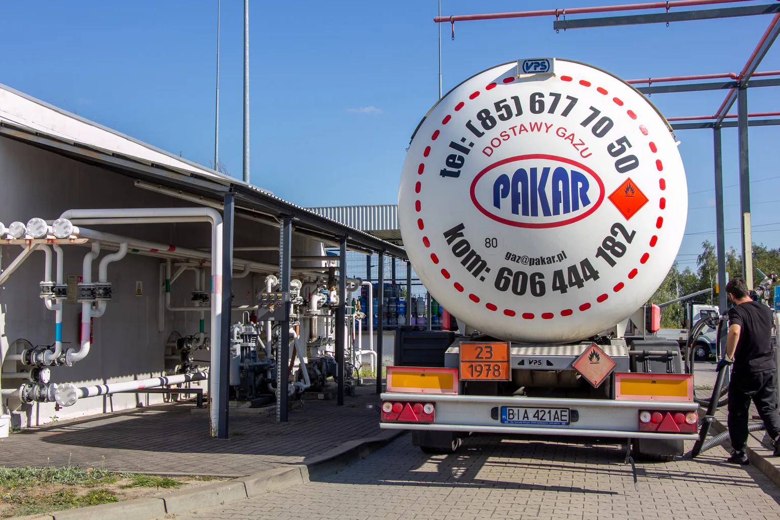 Naczepa-cysterna PAKAR przy stanowisku przeładunkowym terminala LPG: po lewej rurociągi i armatura pod zadaszeniem, po prawej pracownik z wężem